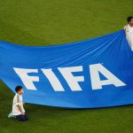 Children hold a banner of the FIFA logo on the pitch before a match