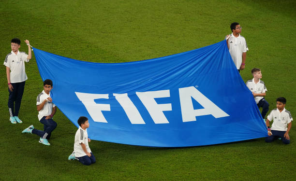 Children hold a banner of the FIFA logo on the pitch before a match